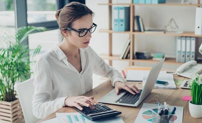 Woman working with laptop and calculator at desk.
