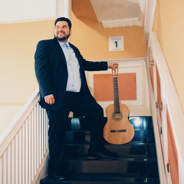 Man in suit holding guitar on stairs.