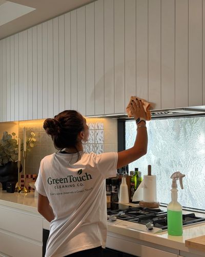 Person cleaning kitchen cabinets wearing a GreenTouch Cleaning Co. shirt.