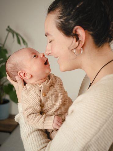 Mother lovingly holds and smiles at her baby dressed in a cozy knit outfit.