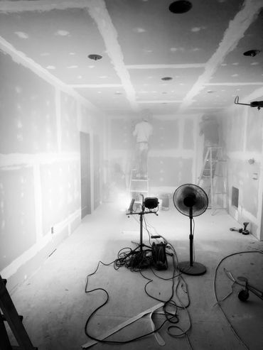 Workers sanding drywall in a dusty room under construction.