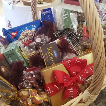 Gift basket filled with assorted snacks and a thank you gift box with a red bow.