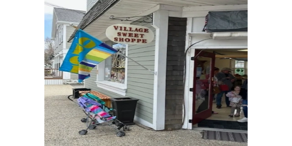 Exterior view of Village Sweet Shoppe with colorful flags and a stroller outside.