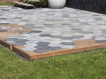 A partially completed hexagonal stone patio in a backyard under wooden stairs.