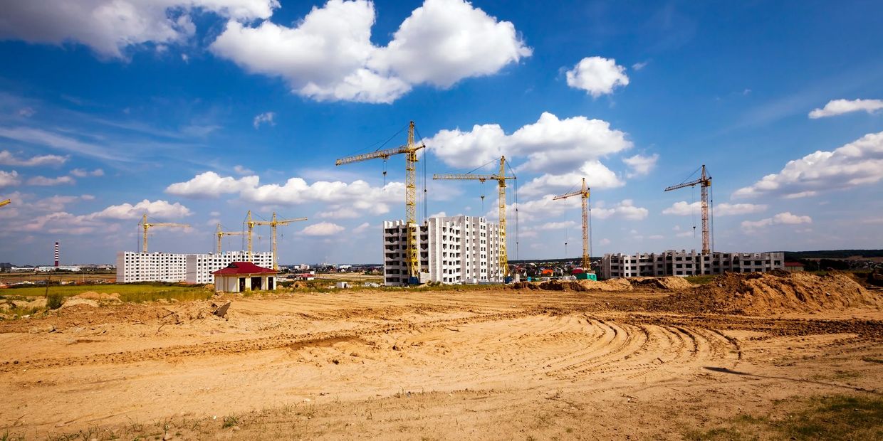 Construction site with cranes and partially built apartment buildings under a blue sky.