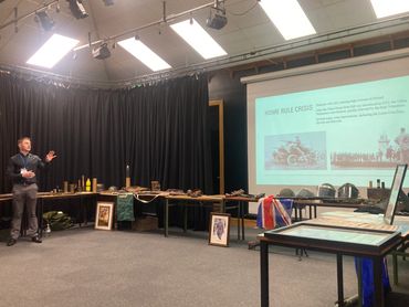 A man giving a presentation on the Home Rule Crisis with historical artifacts displayed.