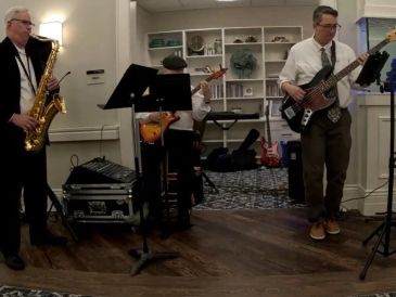 Three musicians playing saxophone, guitar, and bass in a cozy room.