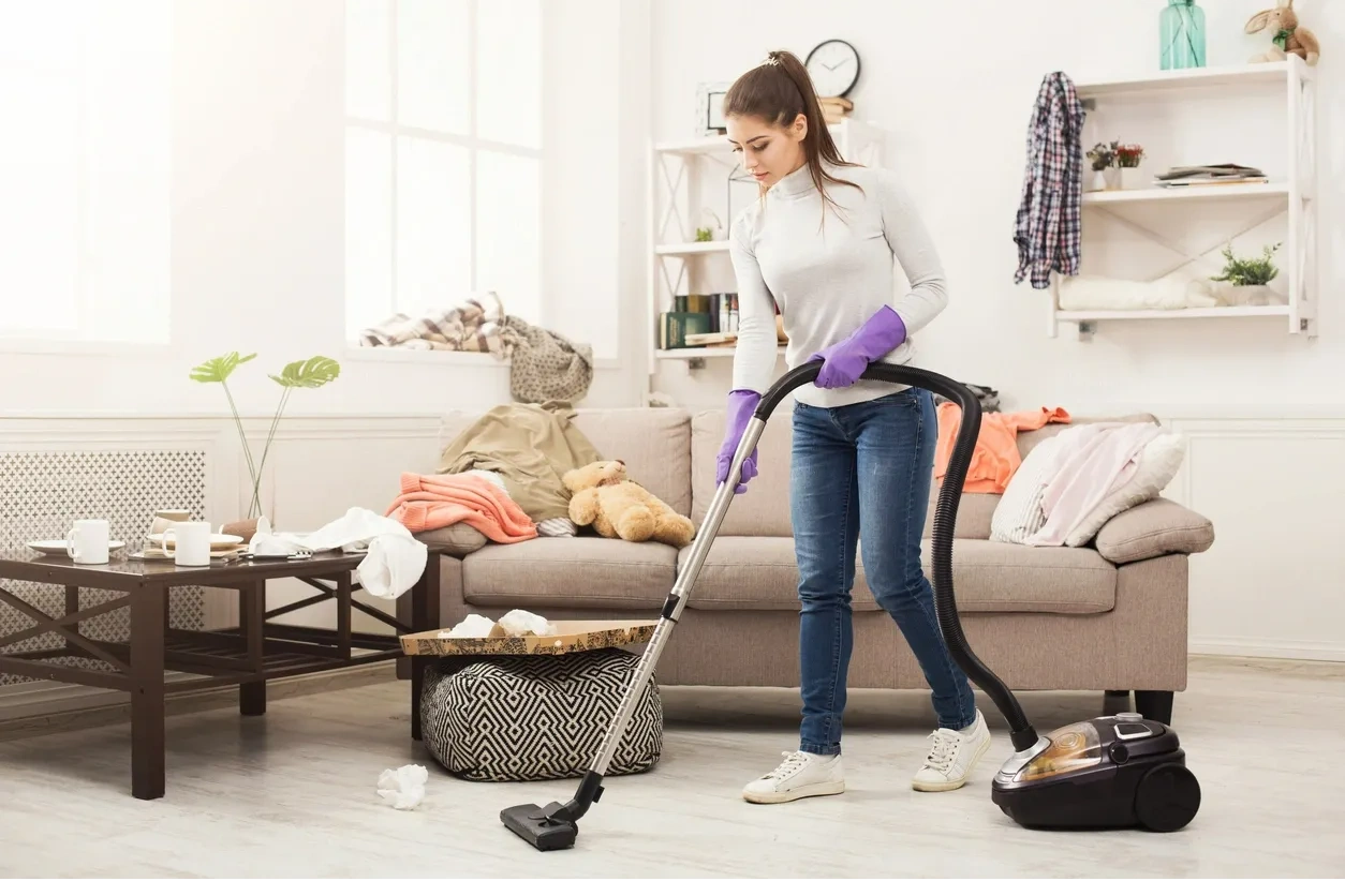 A girl with a vacuum cleaner in her hand with gloves cleaning an area of ​​the house.