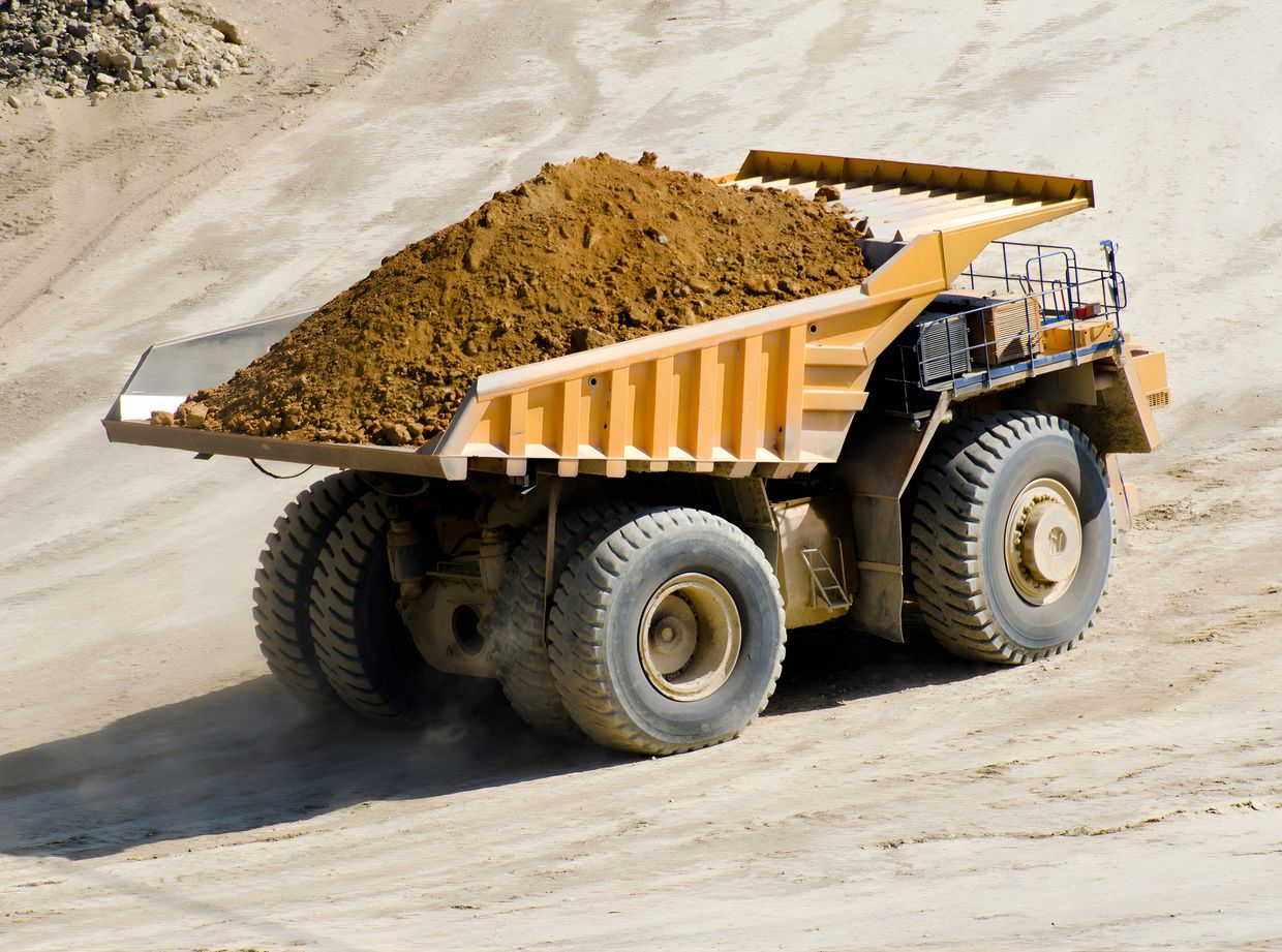 Large mining dump truck loaded with dirt on a sandy quarry road.
