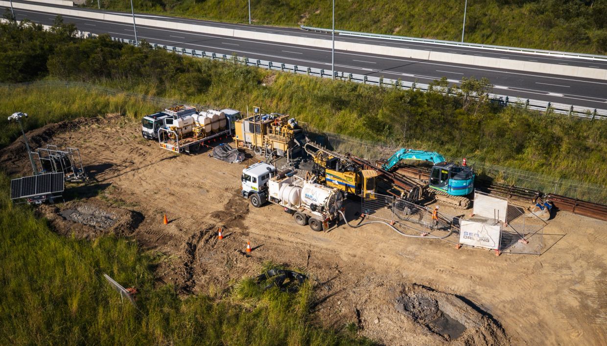 A drilling site near a highway with heavy machinery and trucks.