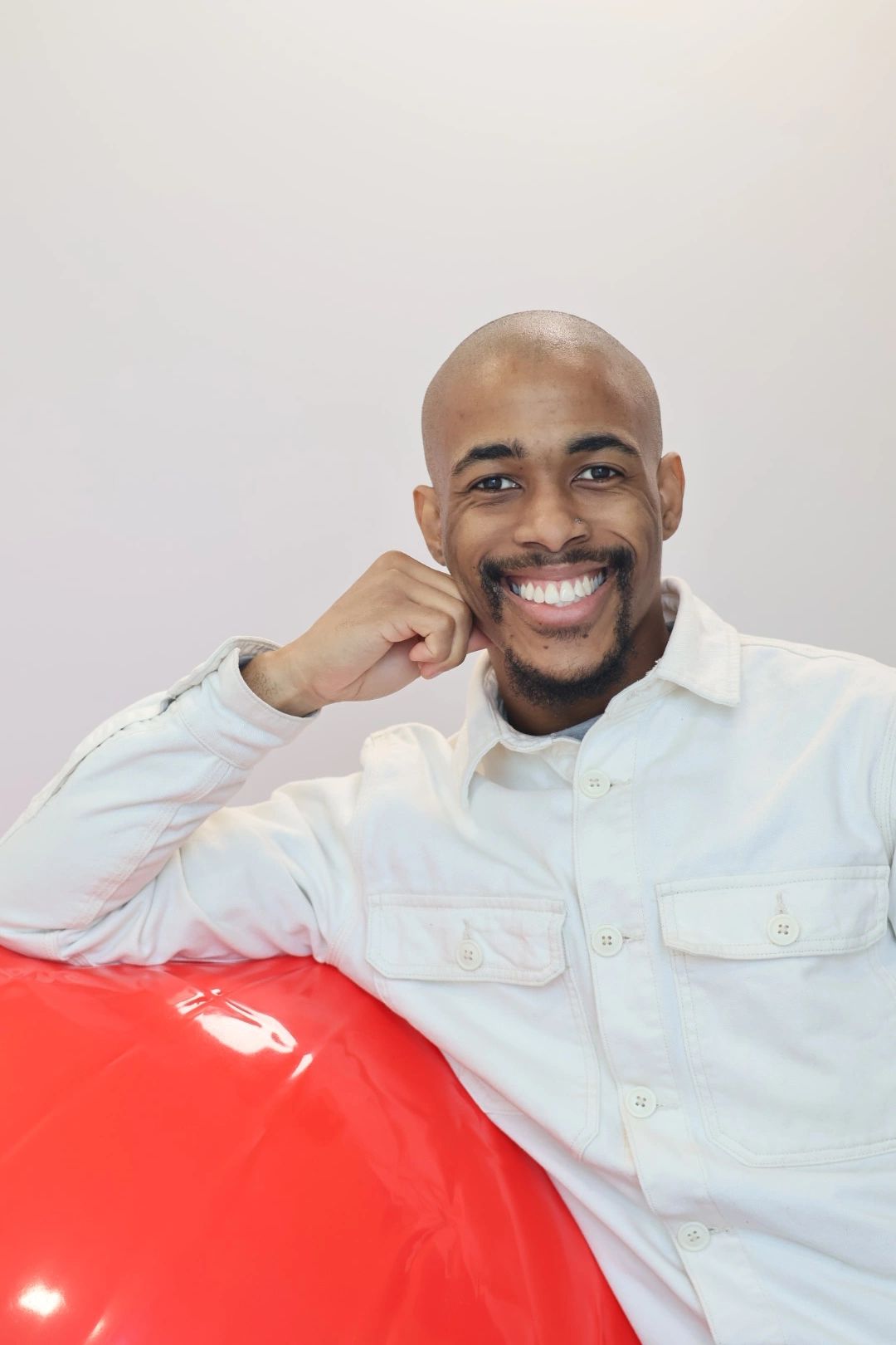 Smiling man in white shirt leaning on a red object.