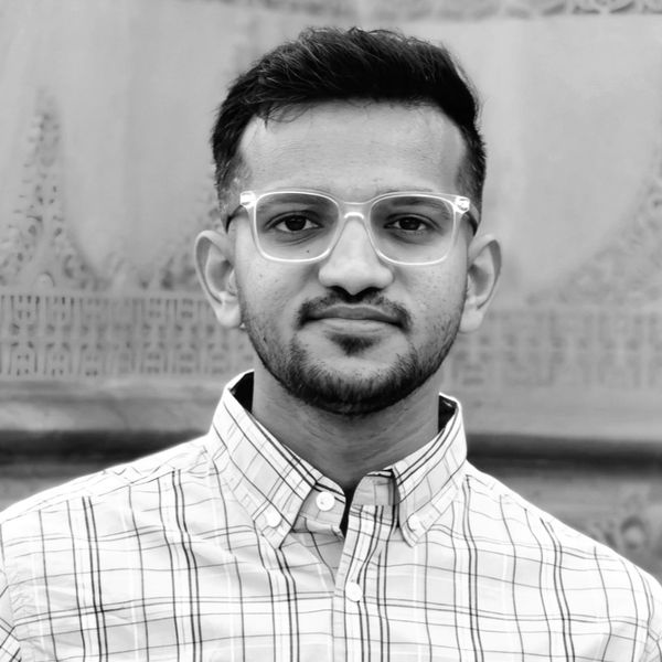 Portrait of a young man wearing clear glasses and a checked shirt, looking at the camera.