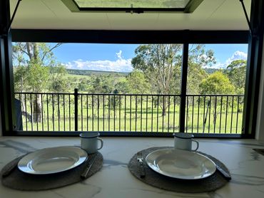A view out a window, overlooking green pastures. Plates and cups are set for dinner on the table.
