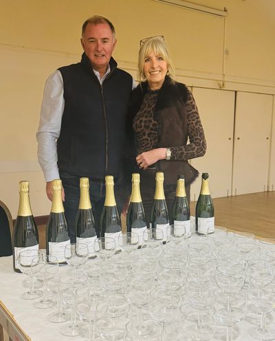 Two people standing behind champagne bottles and glasses.