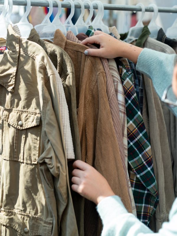 Person browsing various jackets and shirts on hangers at a store rack.