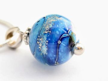 Close-up of a blue glass pendant with silver accents on a white background.
