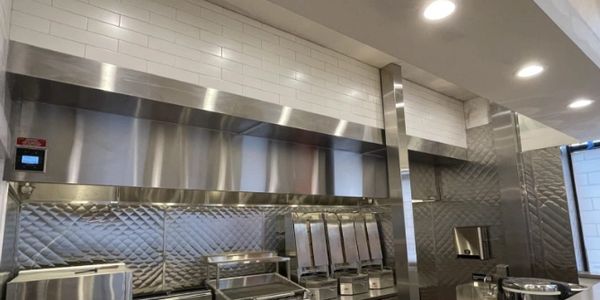 Modern commercial kitchen with stainless steel appliances and white tiled walls.