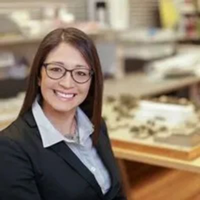 Smiling woman in glasses and business attire in an office setting.