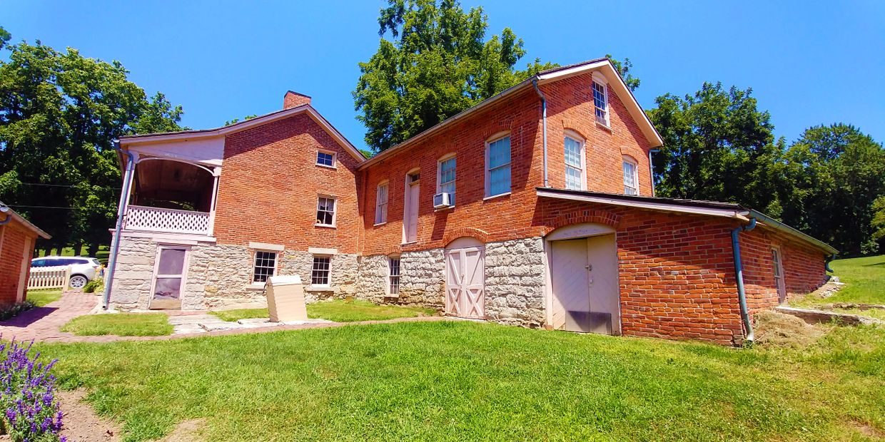 Historic brick and stone house with a green lawn under a clear blue sky.