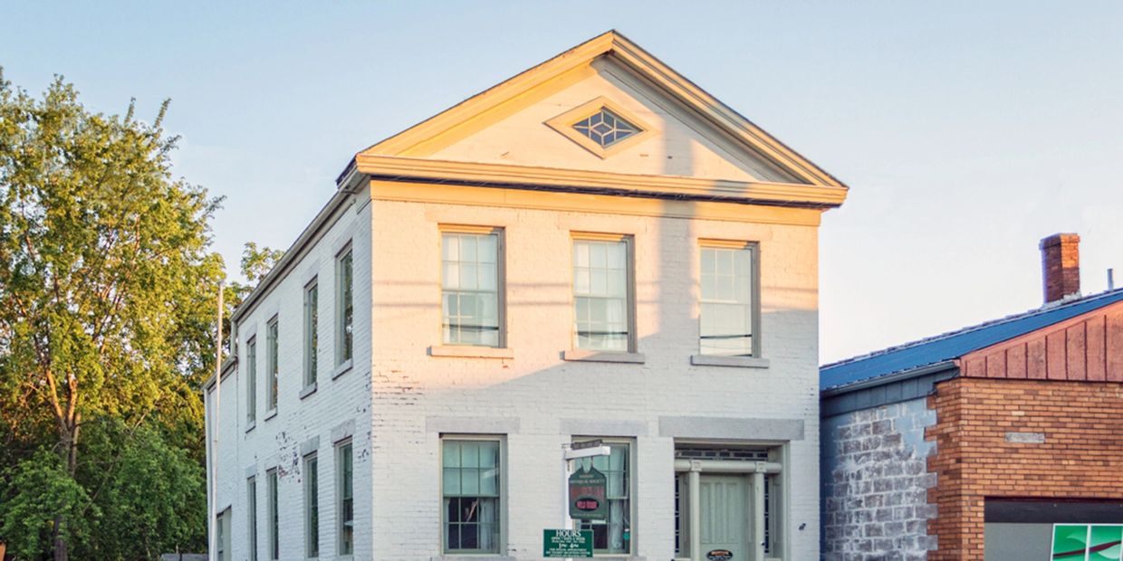 Historic white brick building with green shutters and a bench in front.