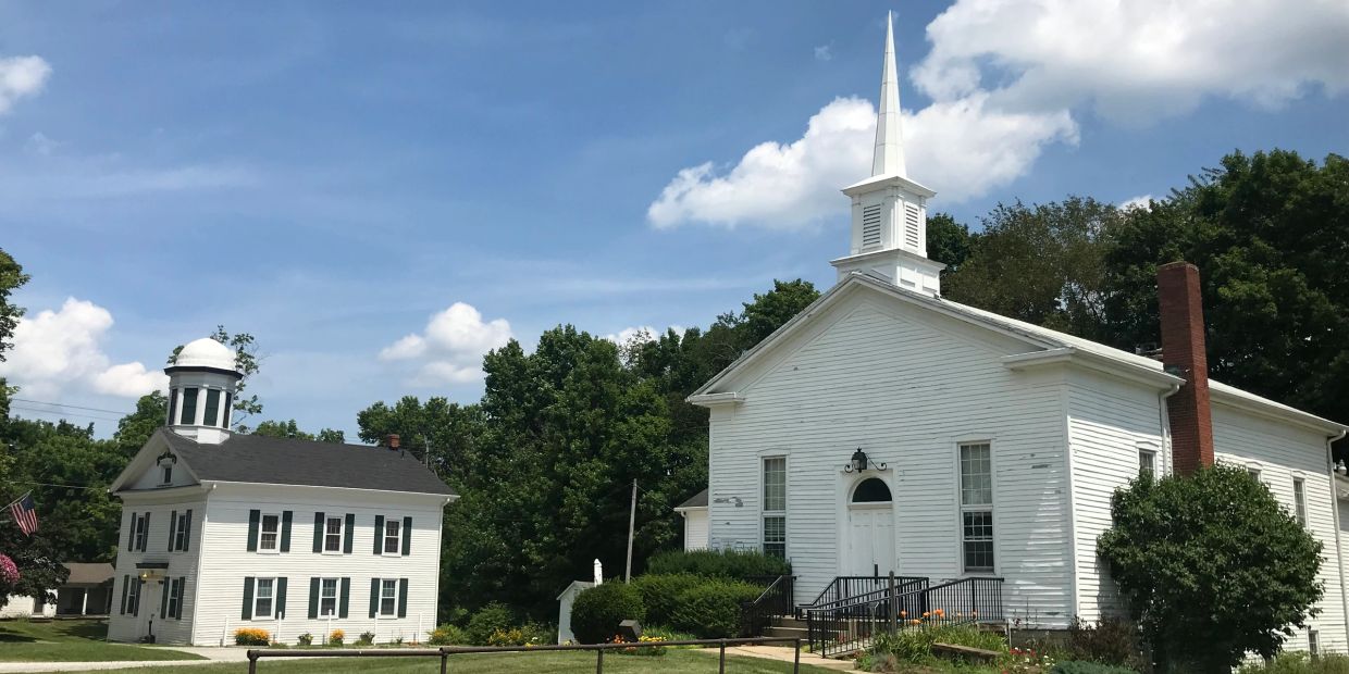 White church and building with trees in background.