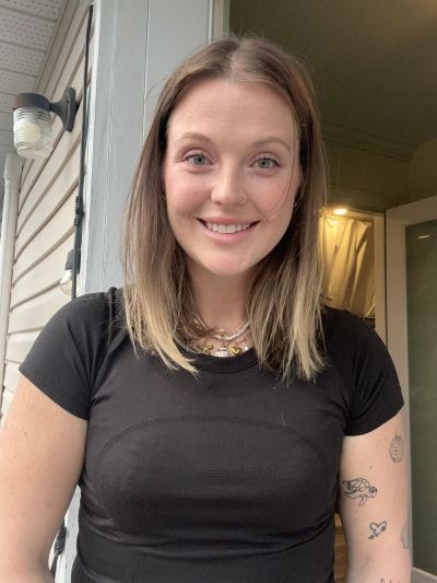 Smiling woman with shoulder-length hair and tattoos on arm.