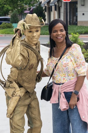 a man dressed as bronze cowboy posing with a female wearing jeans, floral top, and crossbody purse