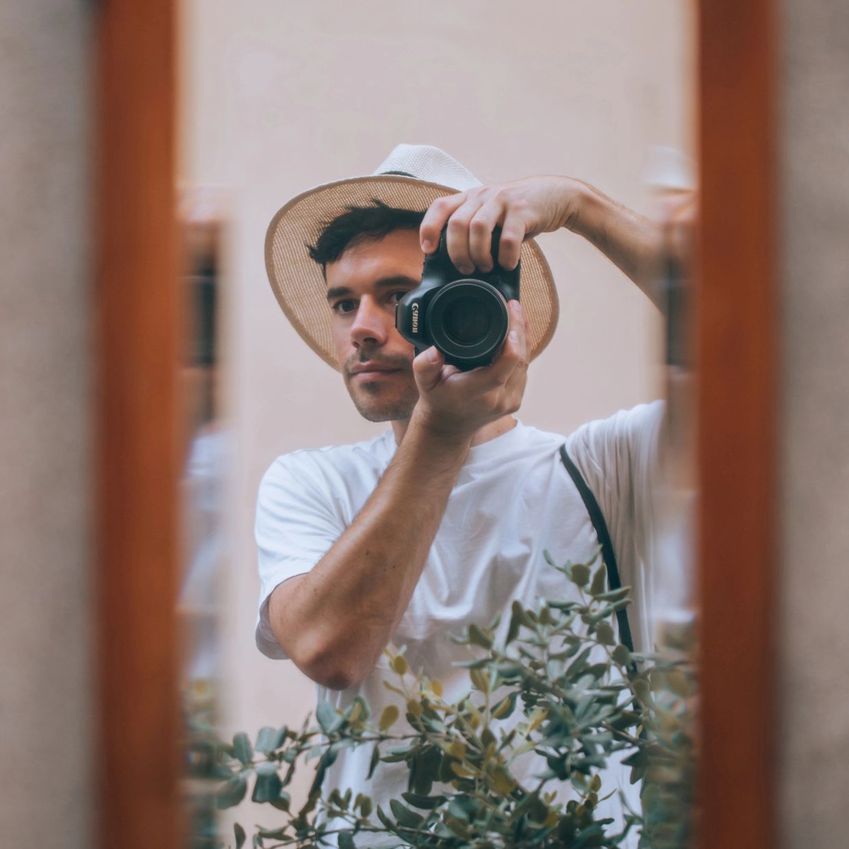 Man with hat taking a mirror selfie with a camera.