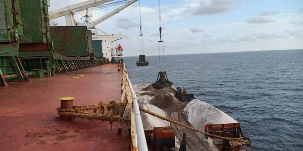 Cargo ship unloading sand onto a barge at sea using cranes.