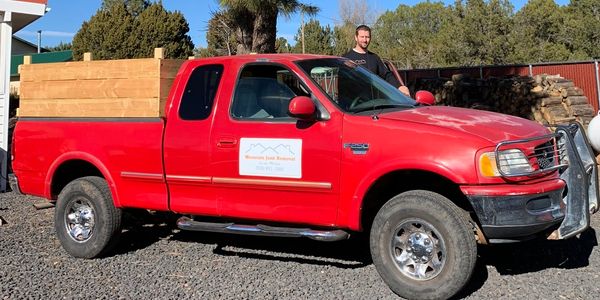 A man standing in the driver side door of a red truck with junk signs and hand built wood walls