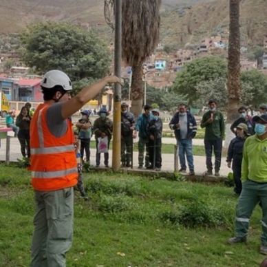 Capacitador en casco y chaleco naranja dirigiéndose a grupo en parque.