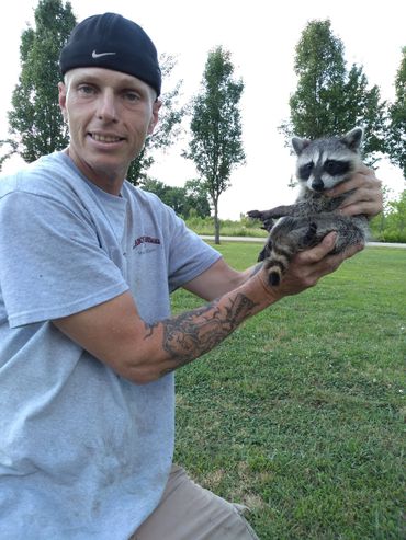 Man holding a raccoon outdoors on a grassy field.