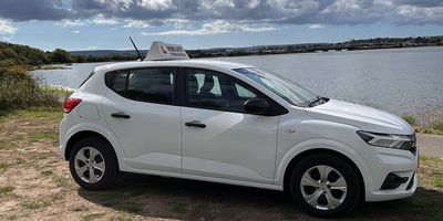 White driving school car parked near water.