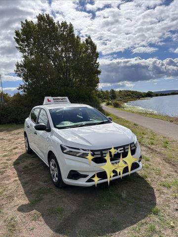 White driving school car parked near a lakeside path.