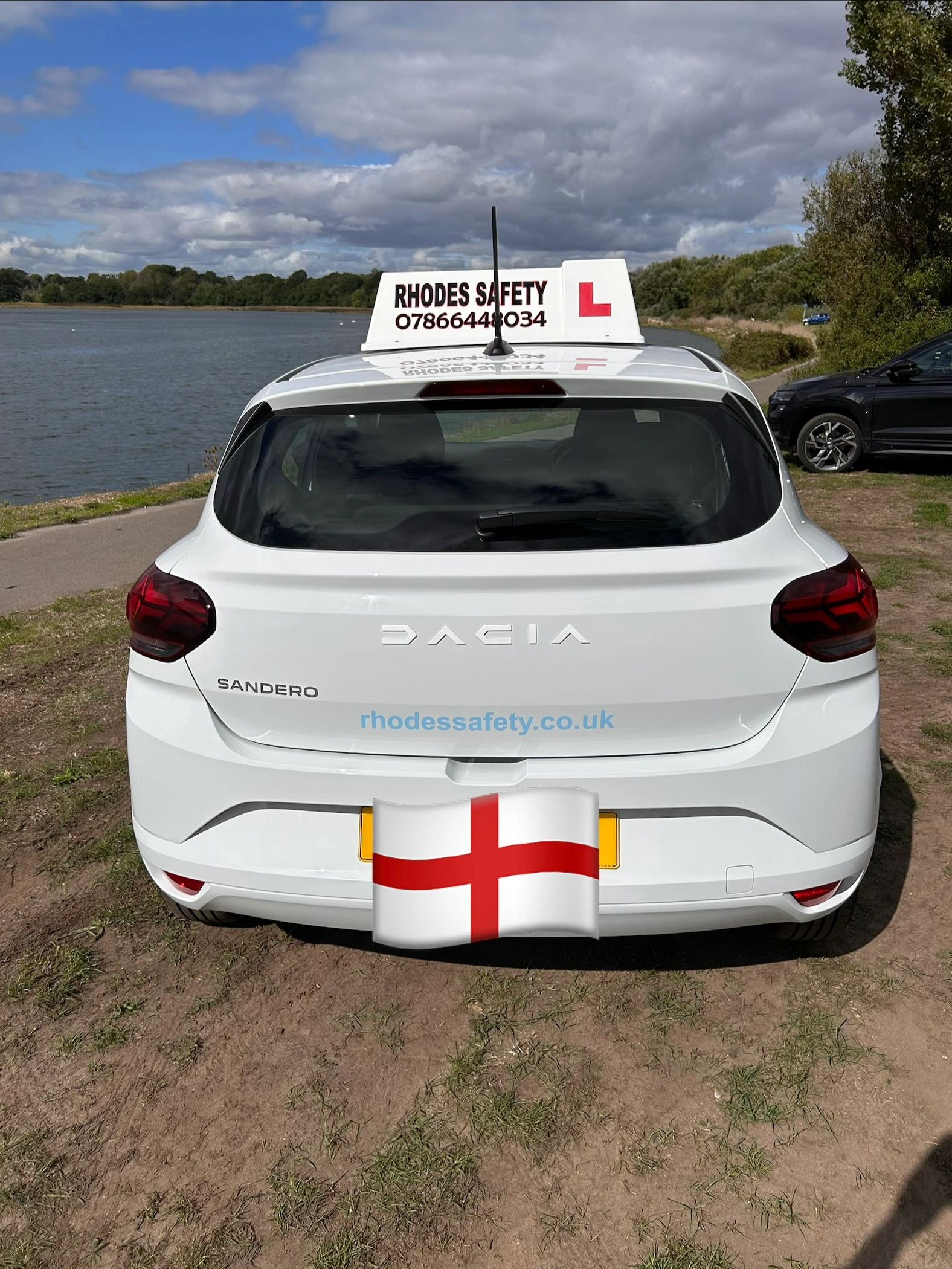 Rear view of a white Dacia Sandero learner car by a lake.