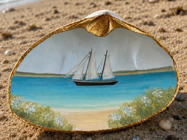 Sailboat painted on a seashell on the beach.