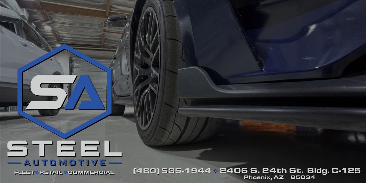 Close-up of a car wheel and Steel Automotive branding in a garage.