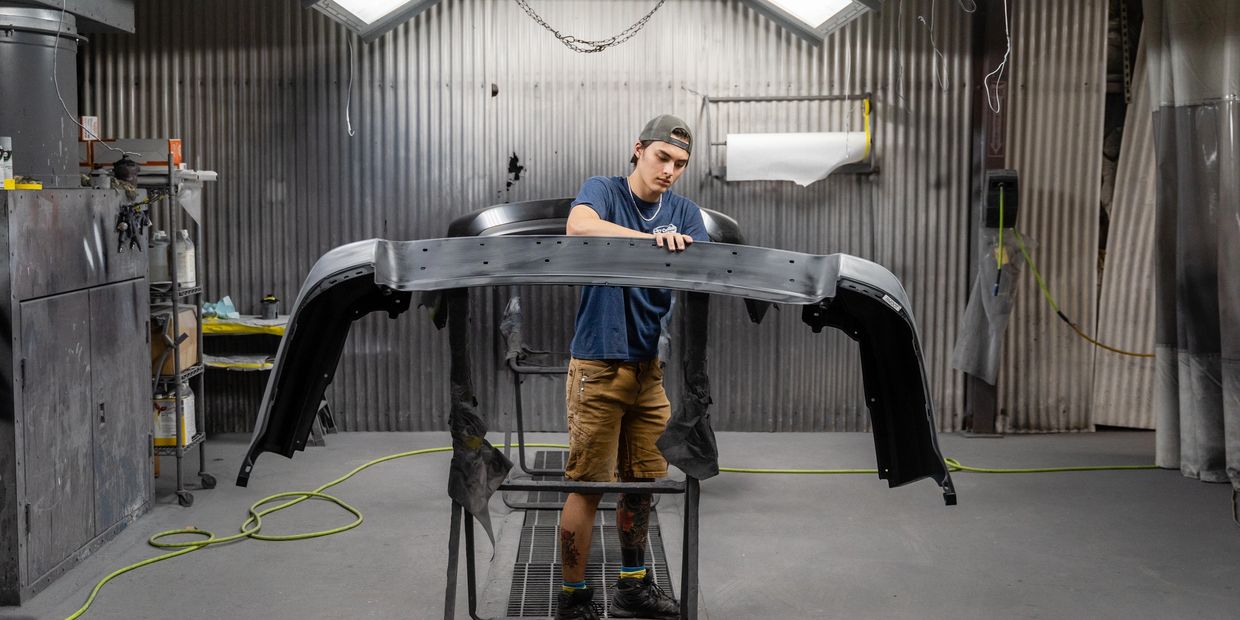 Young man inspecting a car bumper in a workshop.