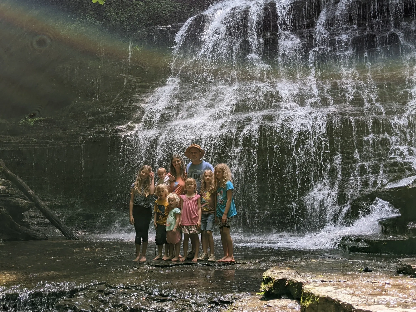 Family posing in front of a cascading waterfall with a faint rainbow above.