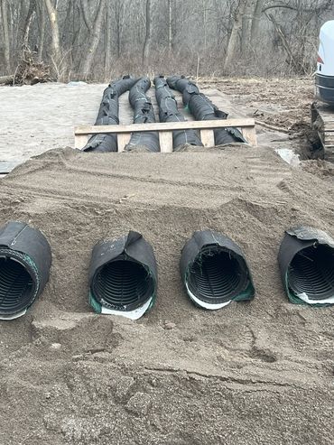 Four large drainage pipes partially buried in sand at a construction site.