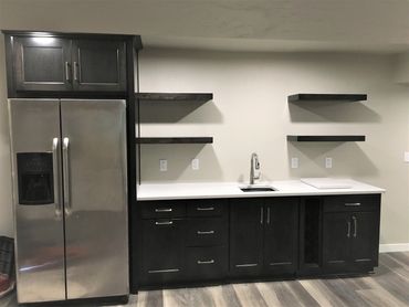 Basement wet bar with full-size refrigerator in a dark stained maple