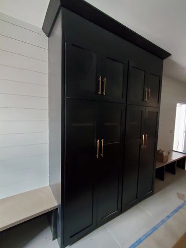New construction mudroom hall with stained benches on both sides of tall cabinets for broom storage