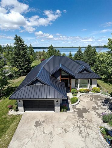 Modern house with black metal roof near a lake and surrounded by greenery.