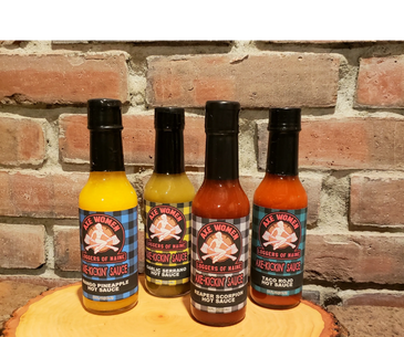 4 bottles of hot sauce on log in front of brick fireplace