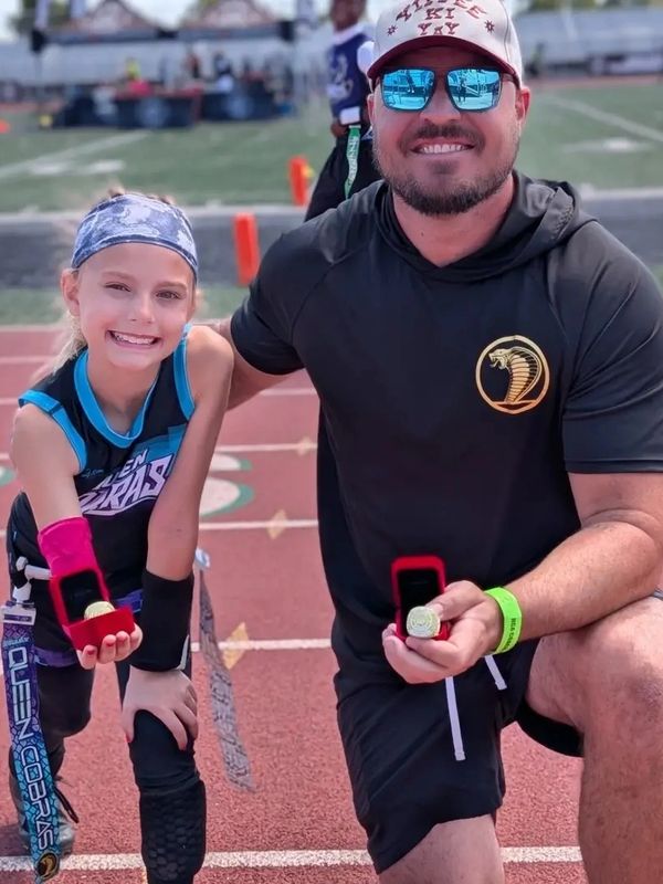 Young athlete and coach proudly showing medals on track field.
