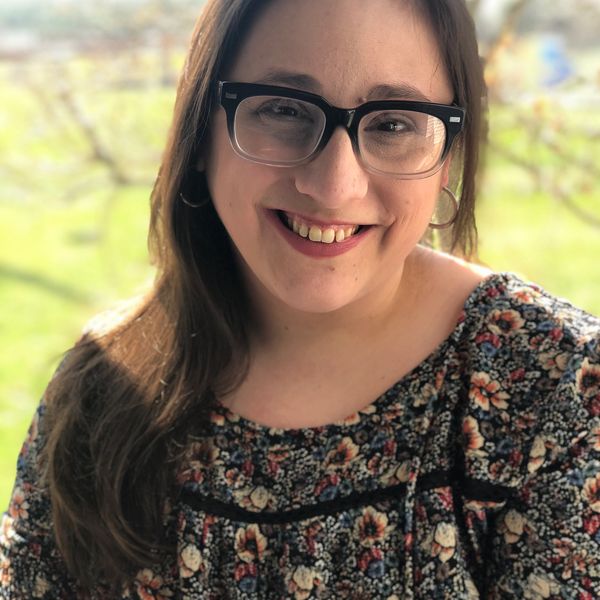 A young woman smiling outdoors with glasses and floral top.
