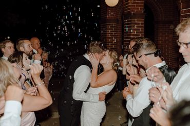 Bride and Groom kissing at formal exit surrounded by guests blowing bubbles