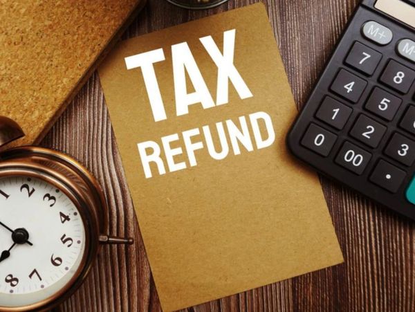 A clock, calculator, and card with 'TAX REFUND' on a wooden table.