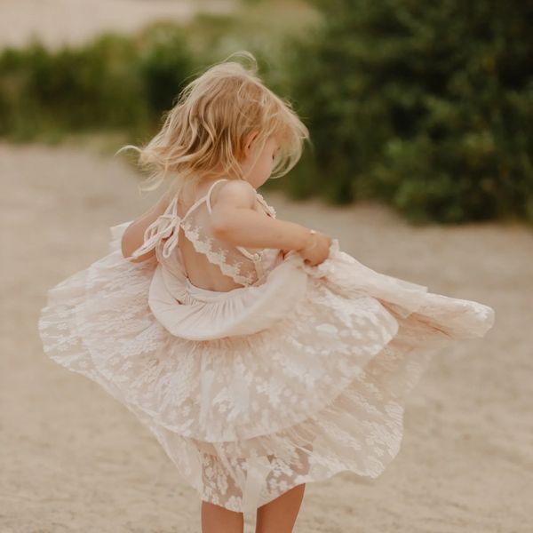 A young girl twirling in a delicate lace dress outdoors.