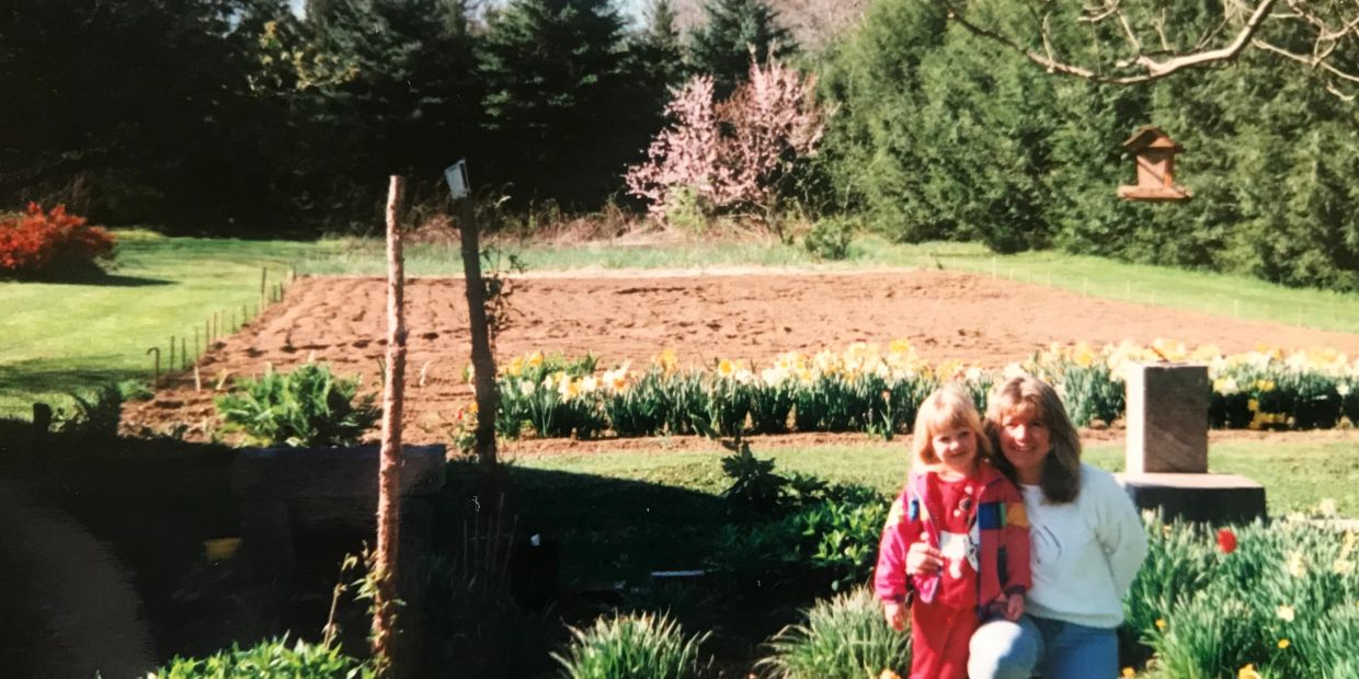 Child and woman smiling in garden with flowers.